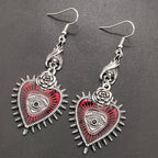Red evil eye heart dangle earrings with rose tops on dark leather, angled view