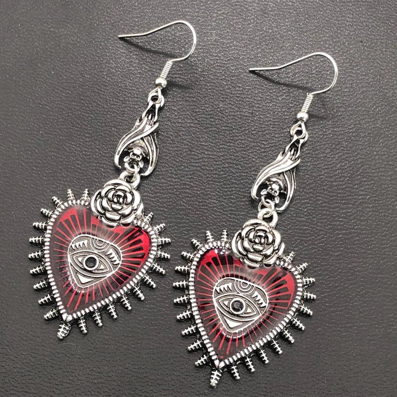 Red evil eye heart dangle earrings with rose tops on dark leather, angled view