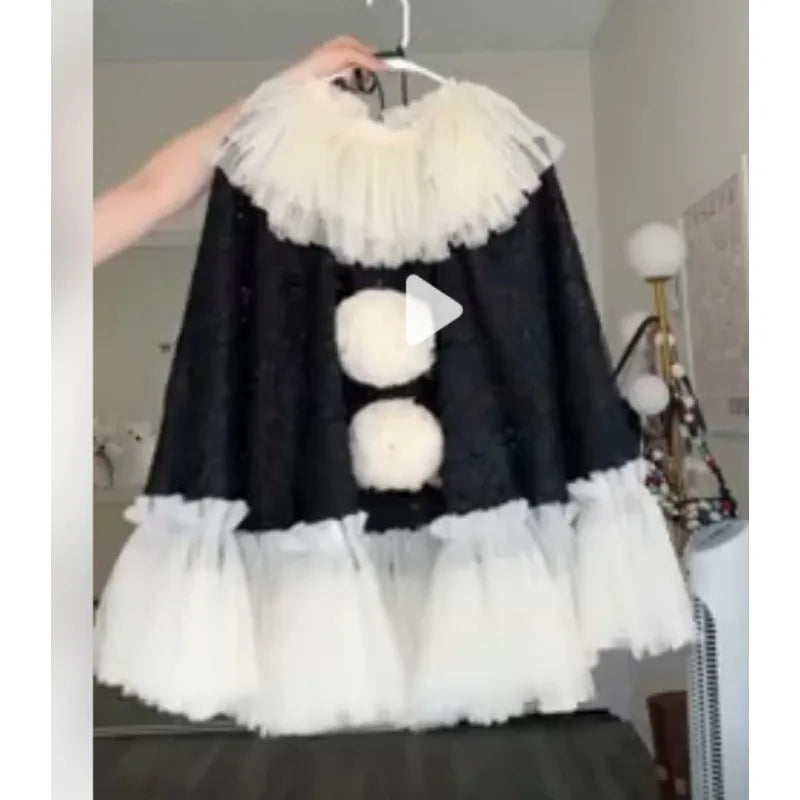 Black velvet pierrot clown poncho with white pom poms and tulle ruffle on hanger, close view