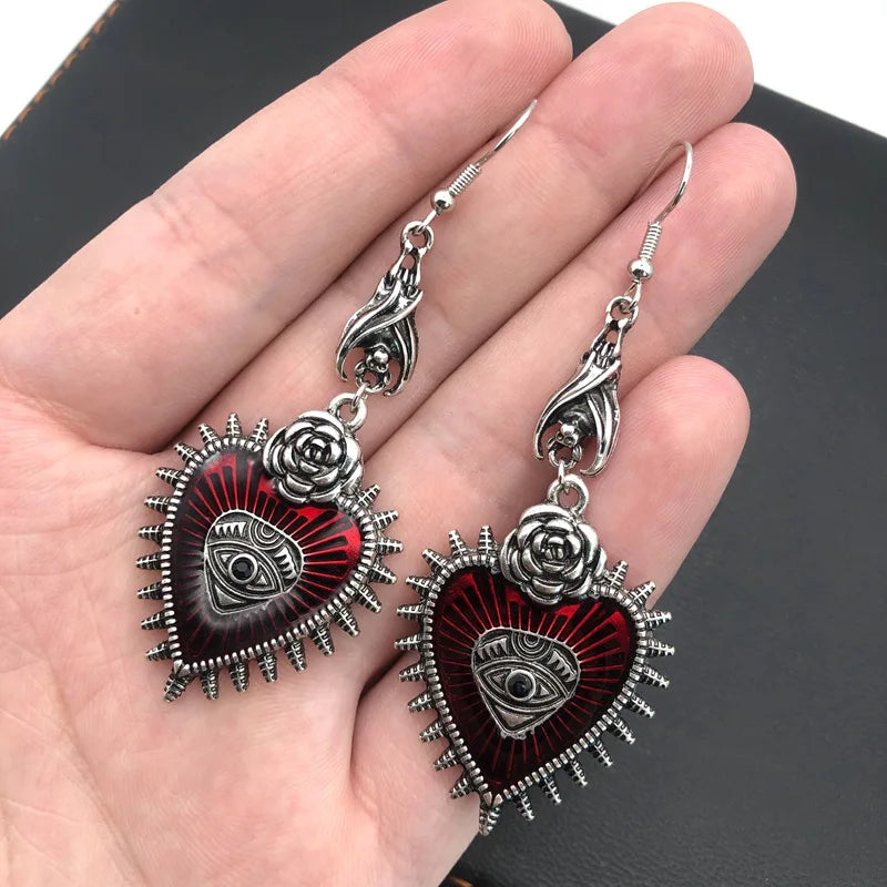 Red evil eye heart earrings with rose and bat wing details held in hand