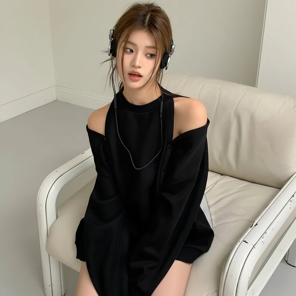 Young woman wearing a black loose fit women's sweatshirt sitting on a white couch with headphones