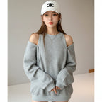 Gray loose fit women's sweatshirt with button shoulder detail worn by model with white cap indoors