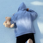 Person wearing a light blue oversized shark pullover hoodie lying on the ground holding a teddy bear