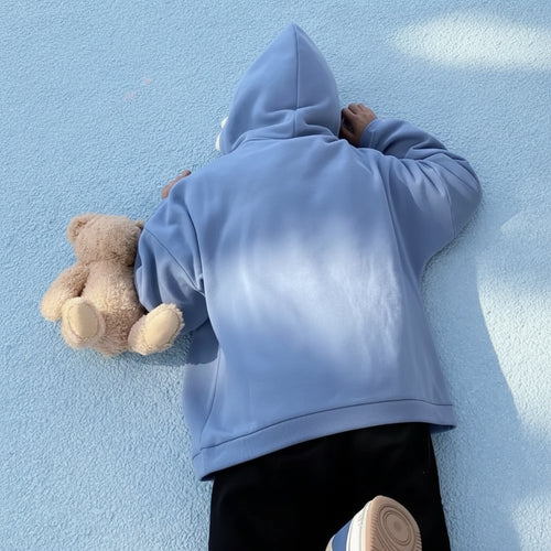 Person wearing a light blue oversized shark pullover hoodie lying on the ground holding a teddy bear