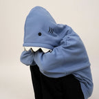 Blue oversized shark pullover hoodie with shark teeth design on the hood worn by person sitting