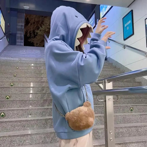 Person wearing oversized shark pullover hoodie in blue with shark teeth hood design on stairs