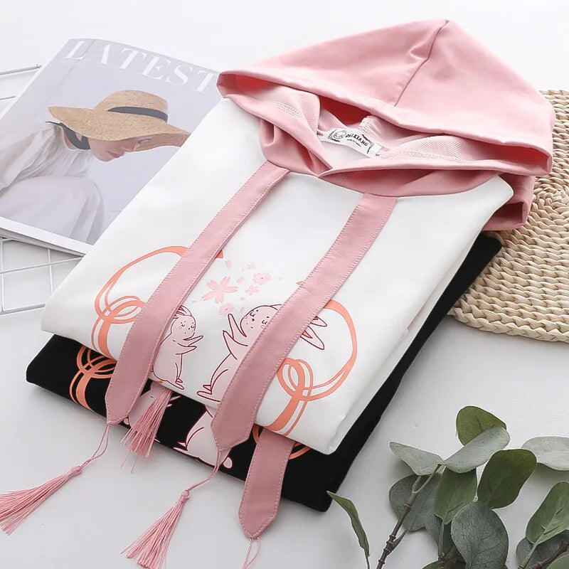 Casual japanese cute hoodie with cartoon print in white and pink folded on a table