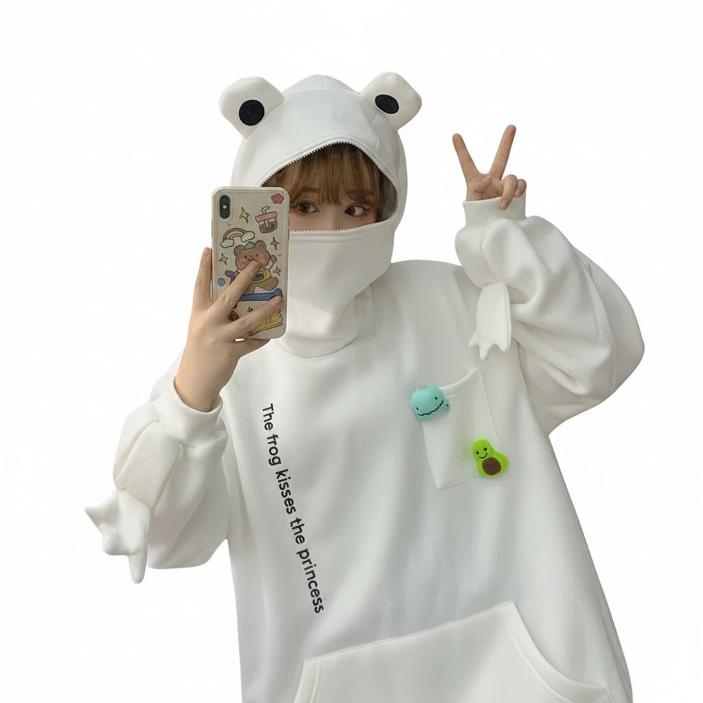 Person wearing a white cute frog pullover sweatshirt with frog eyes on the hood and small frog decorations on the pocket