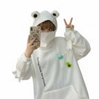 Person wearing a white cute frog pullover sweatshirt with frog eyes on the hood and small frog decorations on the pocket