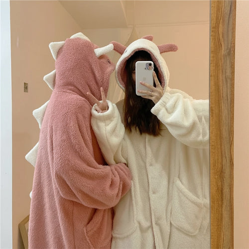 Two women wearing cute hooded pajamas for women in soft pink dinosaur and white designs taking a mirror selfie