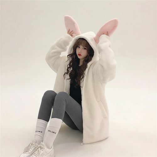 Woman wearing a cute rabbit hooded jacket for women in white with pink ears sitting indoors