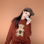 Woman wearing a kawaii style bear sweater for women in brown with bear graphic sitting indoors