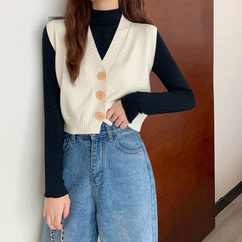 Korean fashion crop knit top in beige with buttons, styled over a black long sleeve shirt and paired with high-waisted jeans