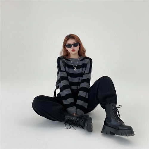 Woman wearing a Korean striped knit sweater in black and gray with black pants and boots sitting on the floor