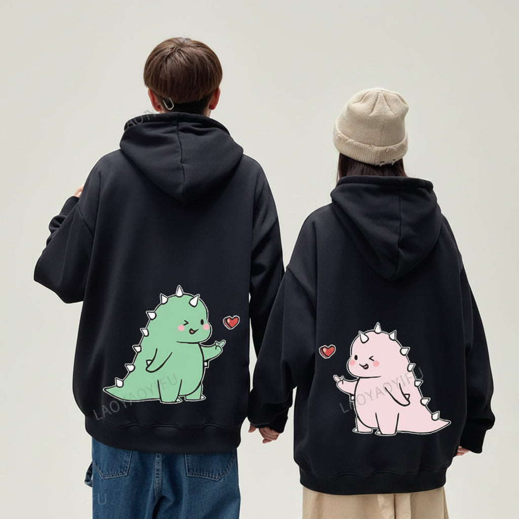 Matching couple hoodies with cartoon design featuring green and pink dinosaur characters on black hoodies
