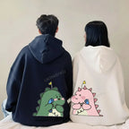 Matching couple hoodies with cartoon design featuring green and pink dinosaurs on black and white hoodies