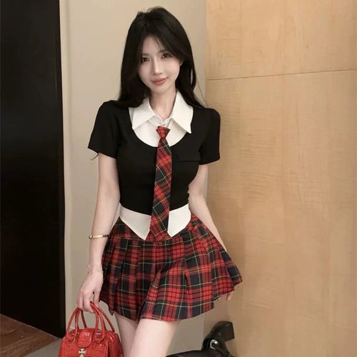Woman wearing a preppy style two piece skirt set with black top, white collar, red plaid skirt and tie holding a red handbag