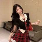 Woman wearing a preppy style two piece skirt set with black top and red plaid skirt indoors