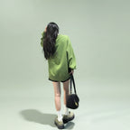 Woman wearing a cute green harajuku design hoodie walking on city street at night with black handbag