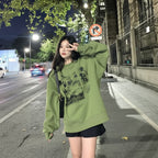 Young woman wearing a cute green harajuku design hoodie posing on a city sidewalk at night