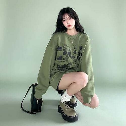Young woman wearing cute green harajuku design hoodie sitting on sidewalk with black bag and beige shoes