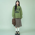 Cute green harajuku design hoodie worn with a checkered skirt and platform shoes on outdoor steps