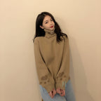 Woman wearing a beige japanese cartoon cat pullover for women with paw prints on sleeves sitting by a wooden table
