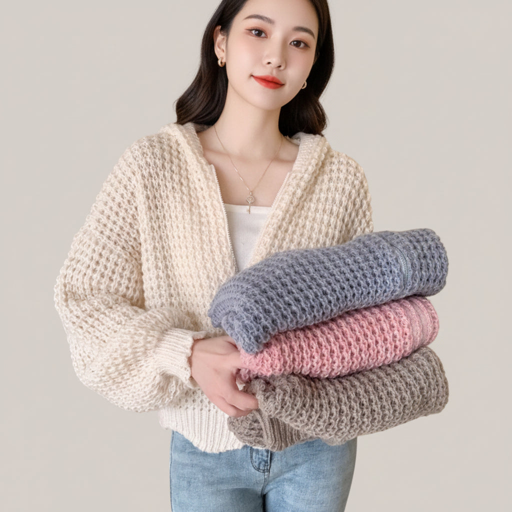 Vusy Kawaii Shop Official cream waffle knit zip-up hoodie with drawstring hood, worn by a person holding folded sweaters in blue, pink, and grey.