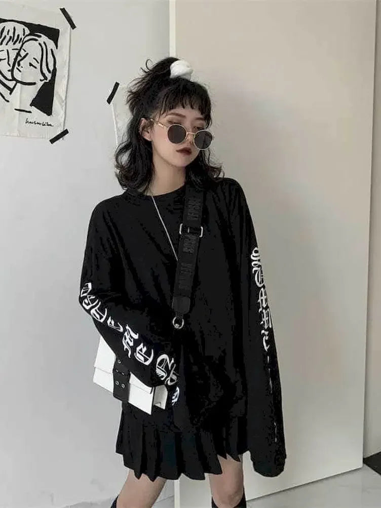 Black women's streetwear anime pullover with white sleeve lettering worn with black pleated skirt and round sunglasses