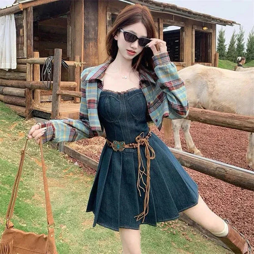 Woman wearing women's ethnic sleeveless summer dress with belt and plaid jacket outdoors near wooden fence